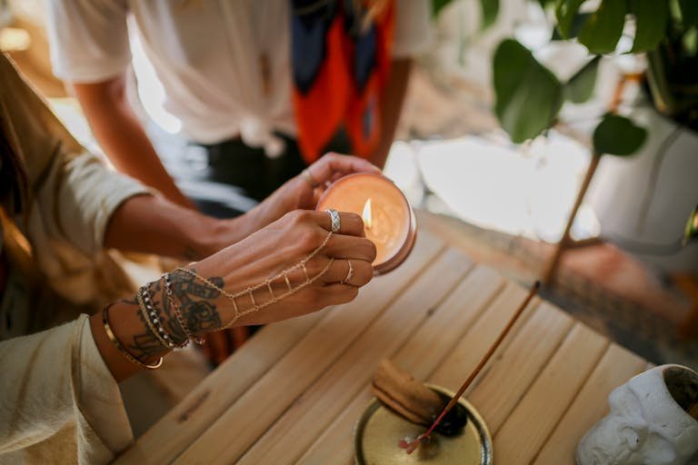 A tattooed hand lights a candle on a wooden surface, promoting relaxation and ambiance.