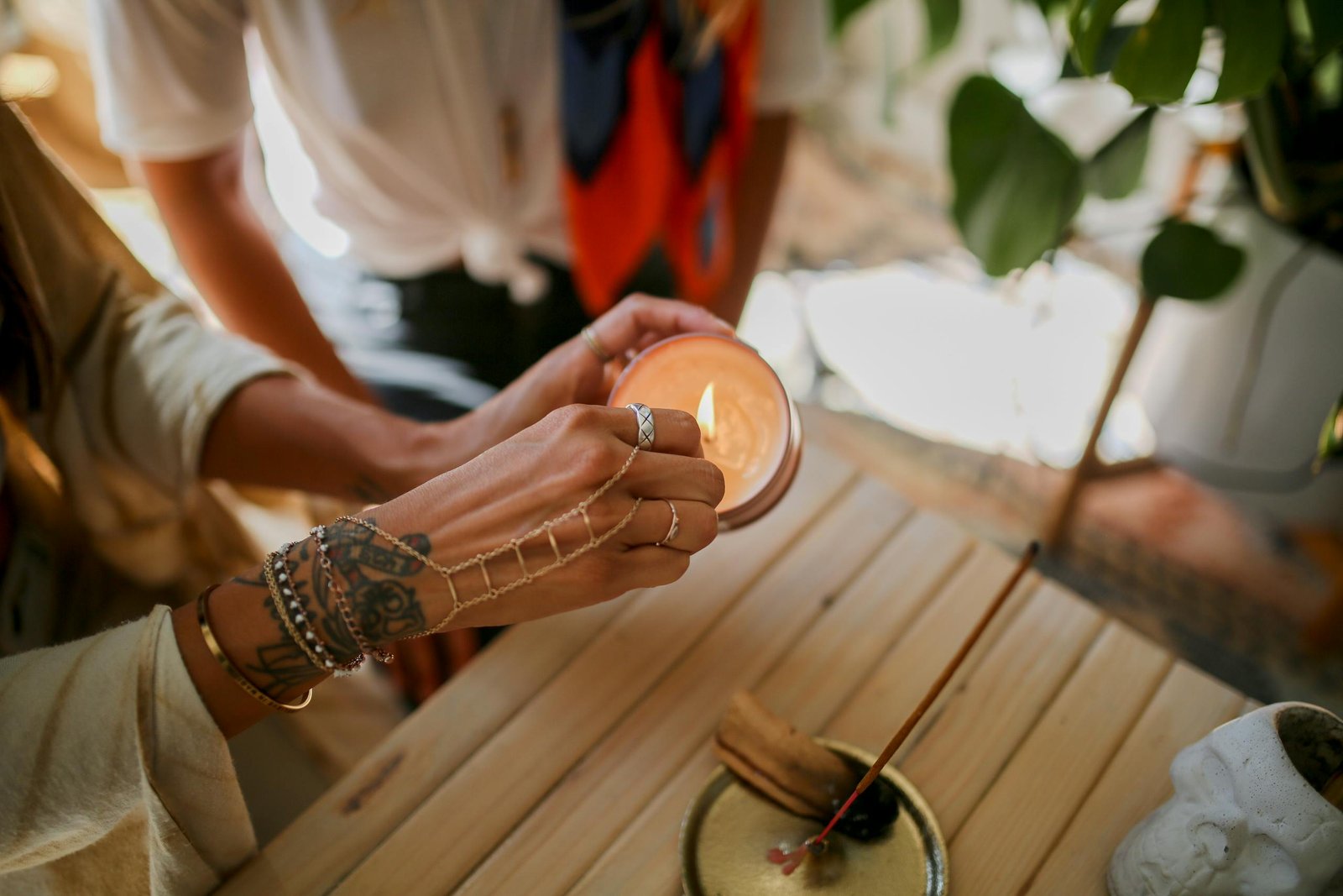 A tattooed hand lights a candle on a wooden surface, promoting relaxation and ambiance.